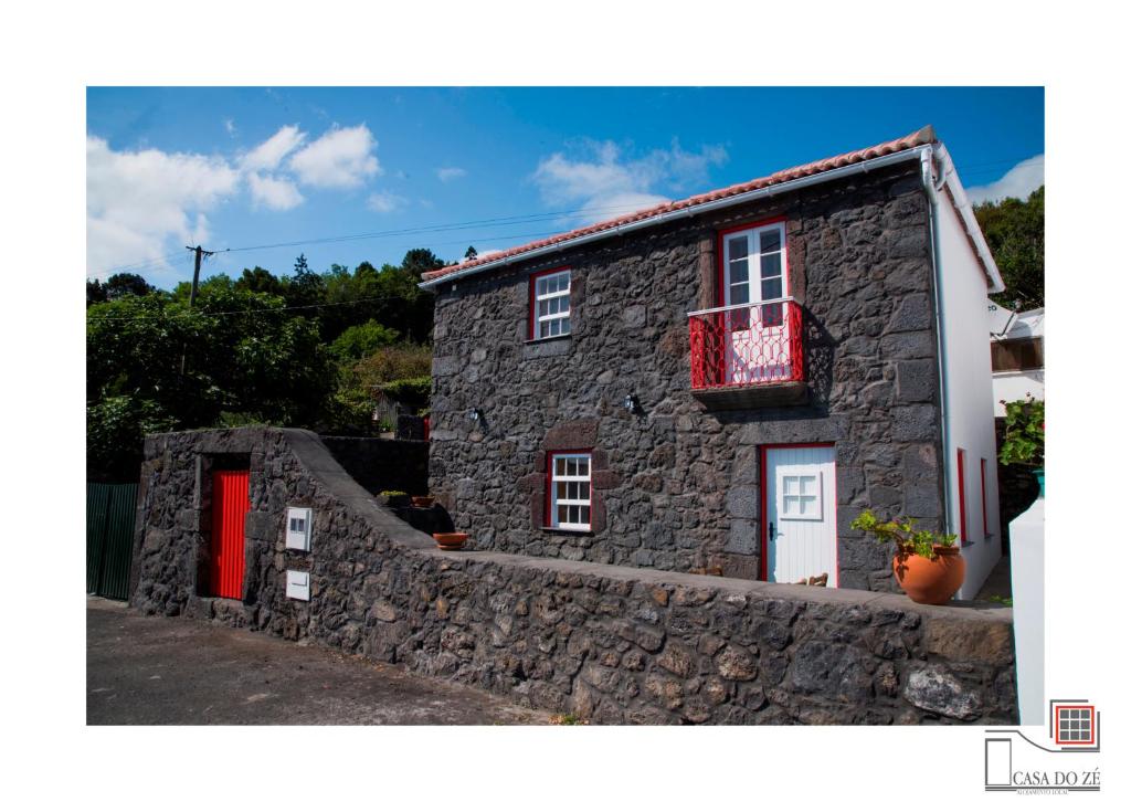 Casa de piedra con puerta roja y pared de piedra en Casa do Zé II AL en Velas