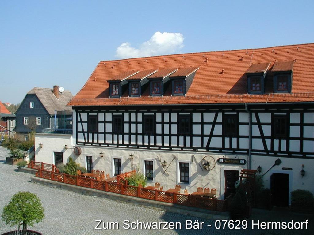 ein schwarzweißes Gebäude mit rotem Dach in der Unterkunft Hotel Zum Schwarzen Bär in Hermsdorf