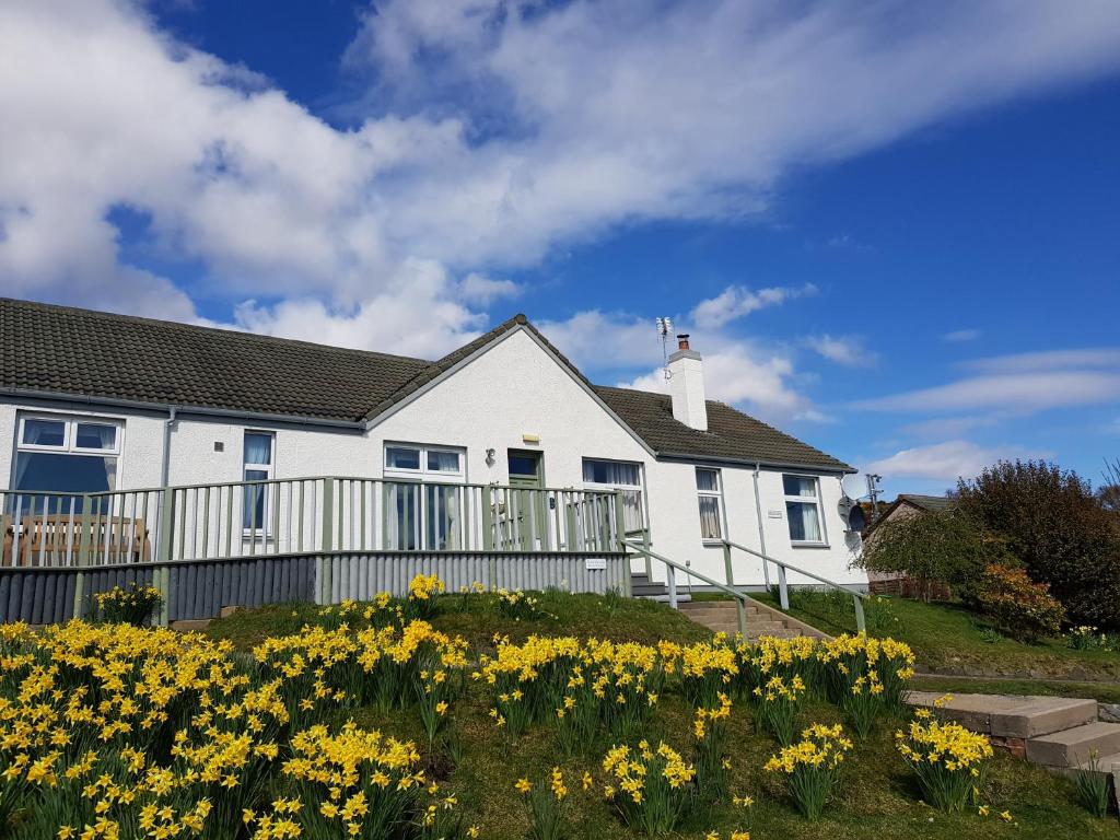 a white house with yellow flowers in front of it at Strathview Lodge in Dornoch