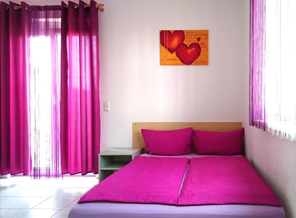 - un lit avec des draps roses dans une chambre avec des rideaux roses dans l'établissement FeWo Gan, à Rust