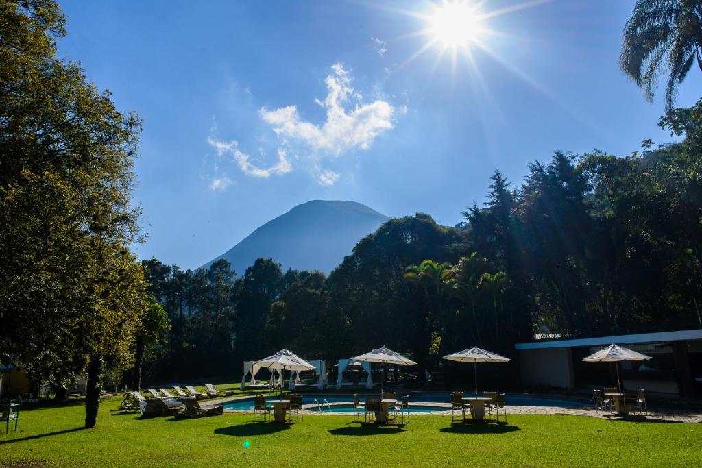 a pool with tables and umbrellas and a mountain at Altenhaus Pousada Itaipava in Itaipava