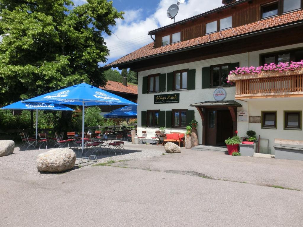 eine Terrasse mit einem blauen Sonnenschirm und Stühlen sowie ein Gebäude in der Unterkunft Goldiger Hirsch in Immenstadt im Allgäu