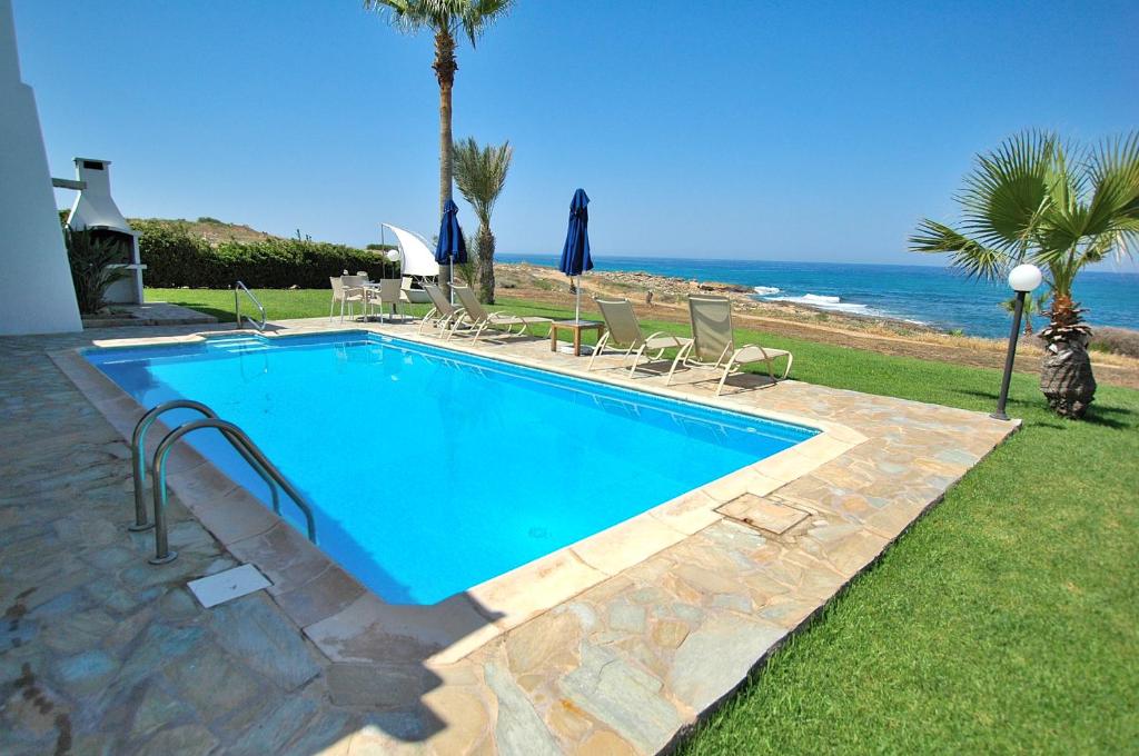 una piscina con sillas y el océano en el fondo en Kymmates Beach Front Villas, en Pafos