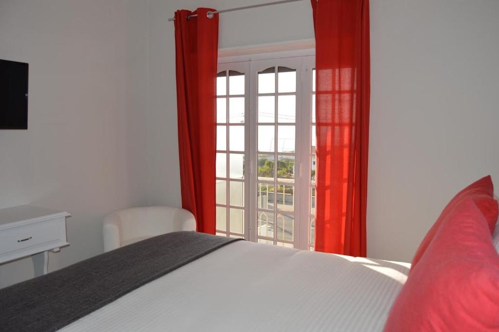 een slaapkamer met een bed en een raam met rode gordijnen bij Casa do Rochedo in Ribamar