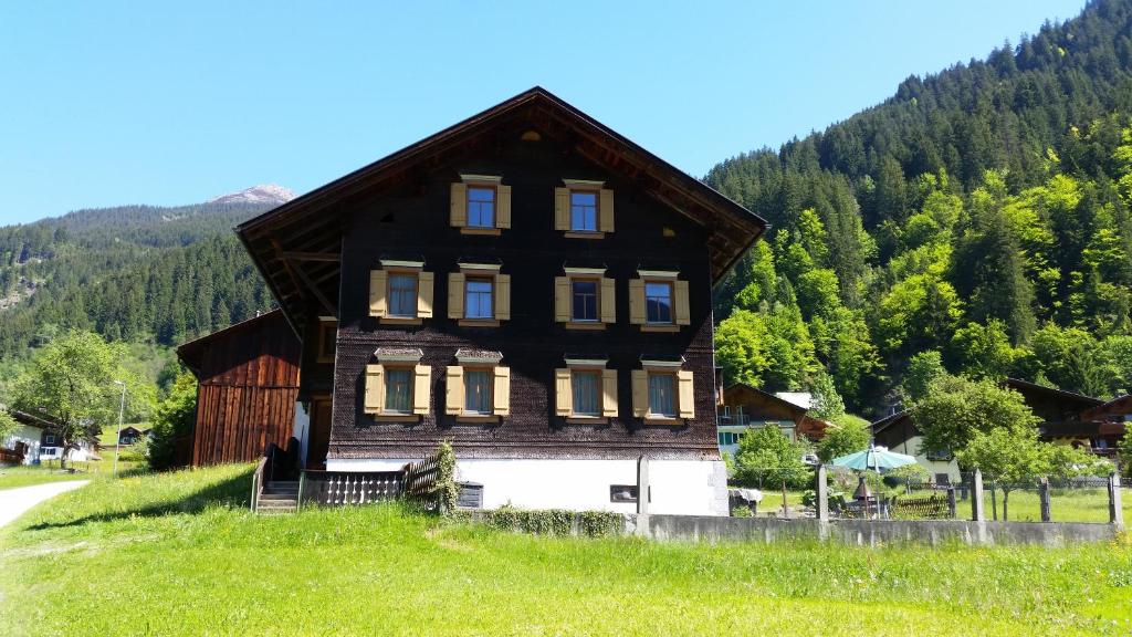 une grande maison en bois sur une colline avec des arbres dans l'établissement Haus Mannhart, à Sankt Gallenkirch