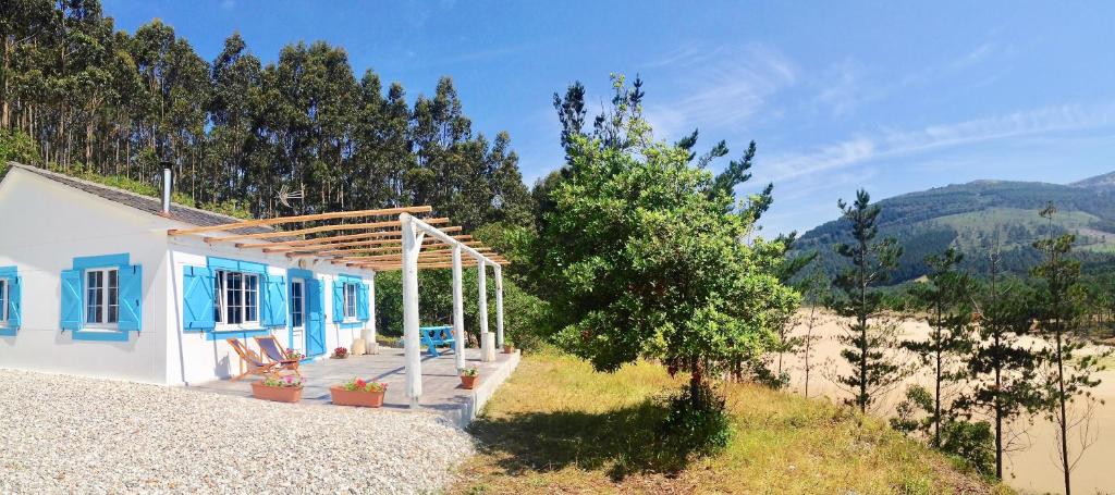 a small white house with blue windows and a hill at Esteiro Surf Lodge in Santa Marta de Ortigueira