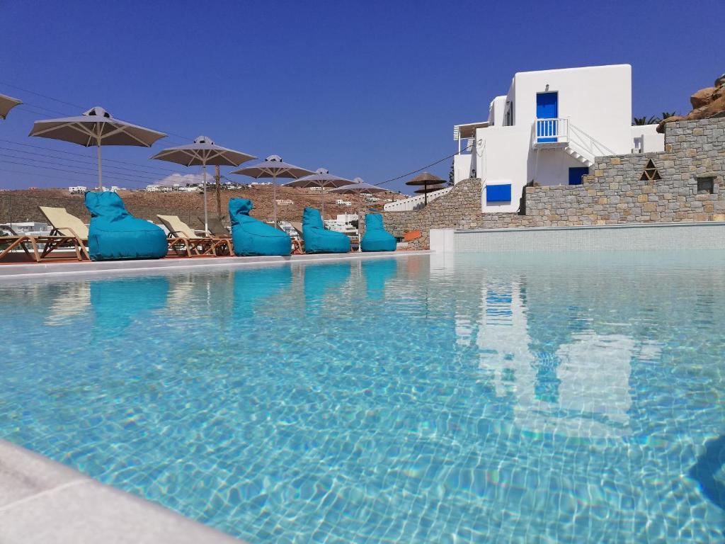 une grande piscine avec des chaises et des parasols bleus dans l'établissement Pelagos Studios, à Platis Gialos