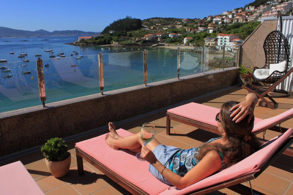 eine Frau, die auf einem Balkon mit einem Glas Wein auf einem Stuhl sitzt in der Unterkunft Hotel Gran Proa Playa Raxó in Raxo