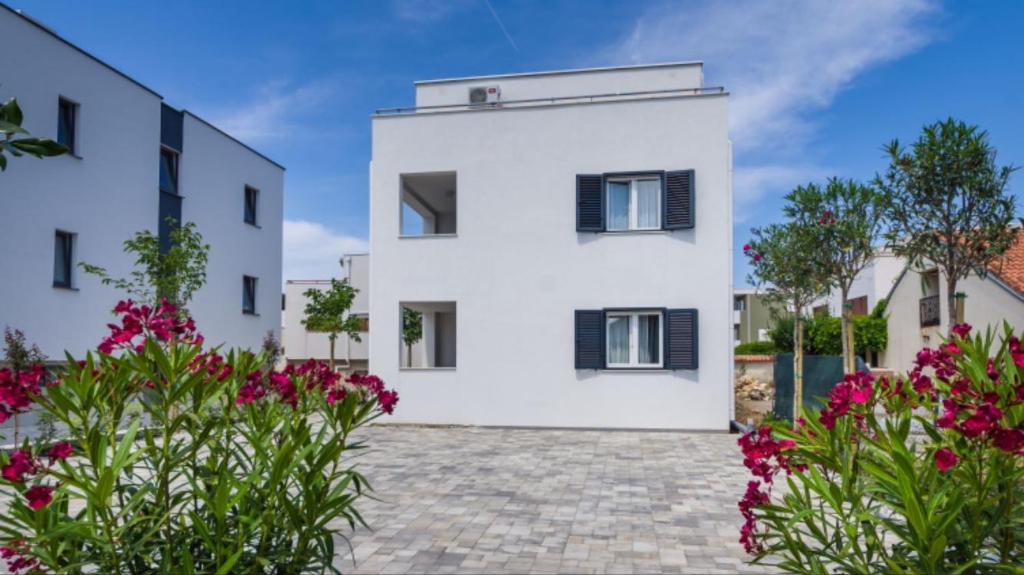 une maison blanche avec des fleurs devant elle dans l'établissement Apartmani Paradise, à Petrčane