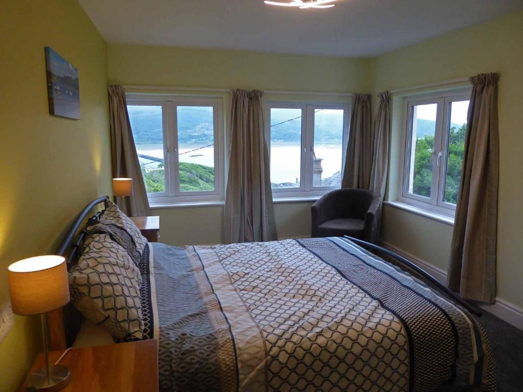a bedroom with a bed with windows and a chair at Bryn Melyn Apartments in Barmouth