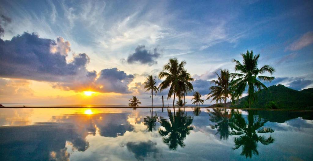 une piscine avec des palmiers et le coucher du soleil en arrière-plan dans l'établissement Siam Sunrise Seaview, à Chaweng