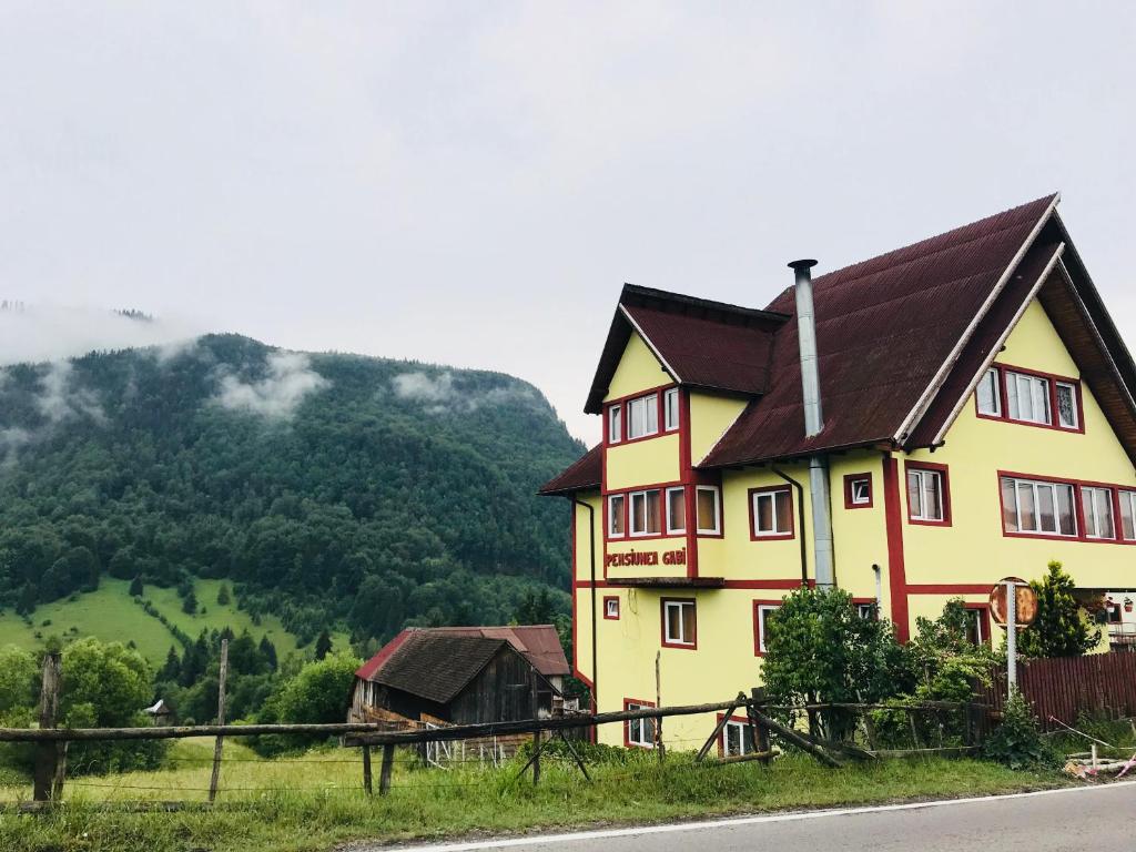 a yellow house with a brown roof on a hill at Pensiunea Gaby in Dîmbovicioara