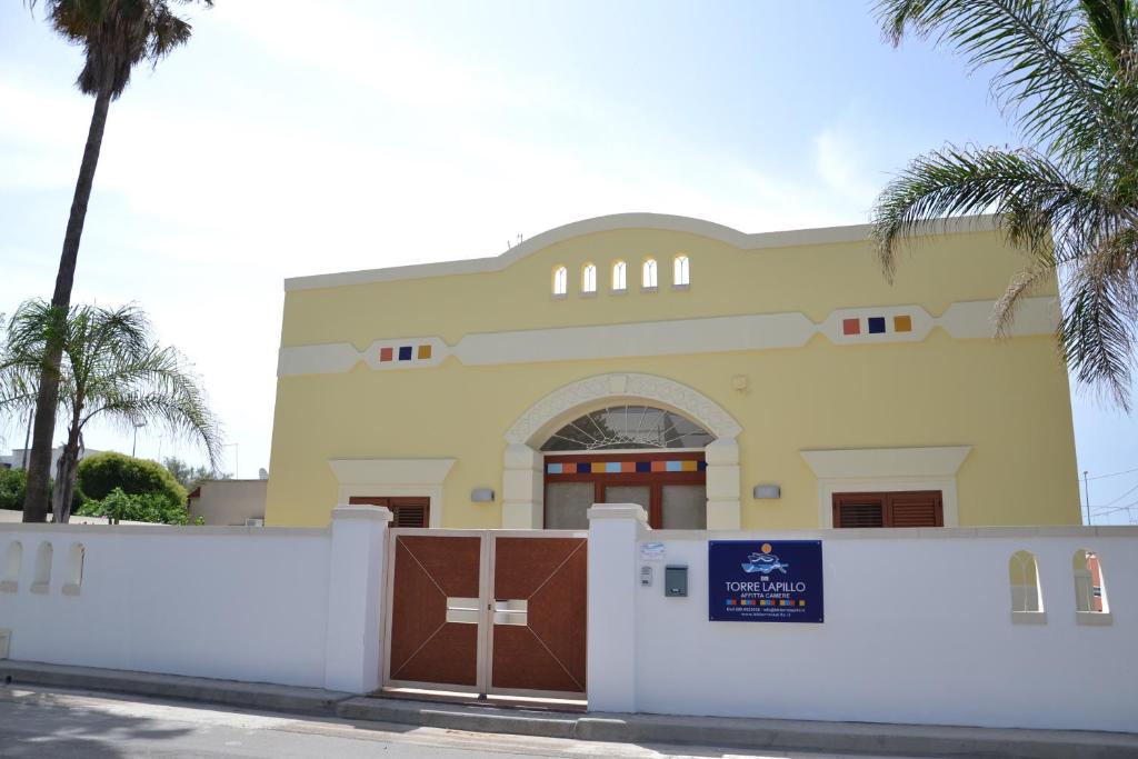 a building with a gate and palm trees at Affittacamere Torre Lapillo in Torre Lapillo