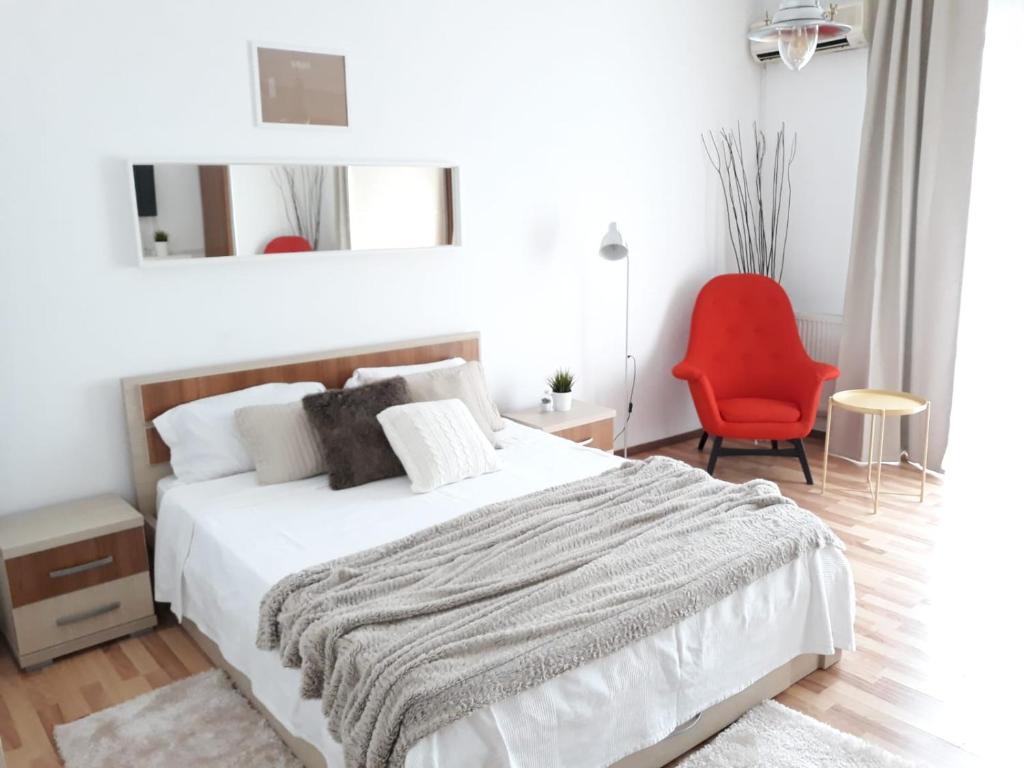 a white bedroom with a bed and a red chair at Studio Old Center in Bucharest