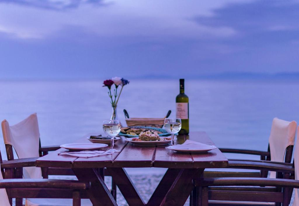 a wooden table with a plate of food and a bottle of wine at Kokkari Beach Hotel in Kokkari
