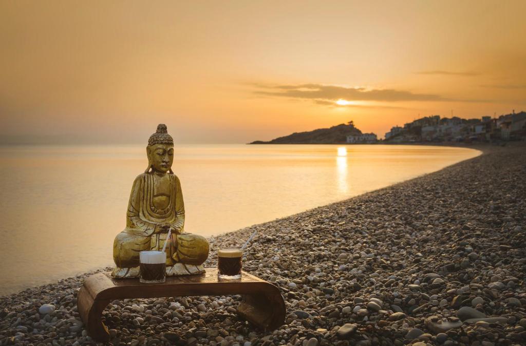 a statue sitting on a beach with two cups at Kokkari Beach Hotel in Kokkari