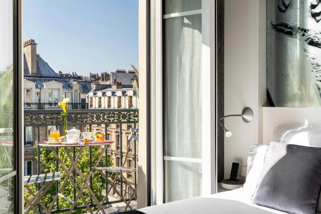 a room with a bed and a balcony with a table at Hotel Marais Grands Boulevards in Paris