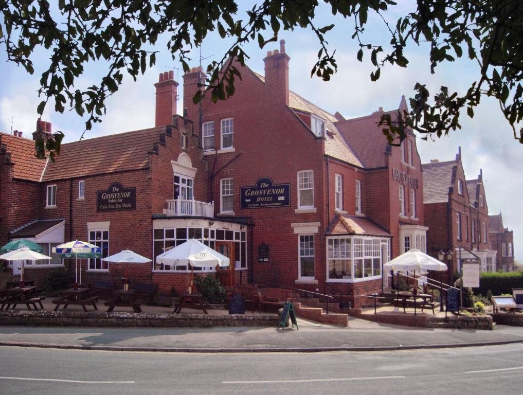 un gran edificio de ladrillo con mesas y sombrillas delante de él en Grosvenor Hotel, en Robin Hood's Bay