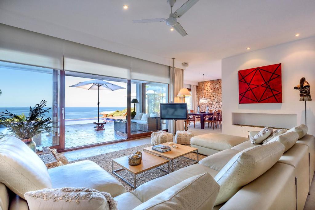 una sala de estar con muebles blancos y vistas al océano. en Villa Can Azul en Cala Tarida
