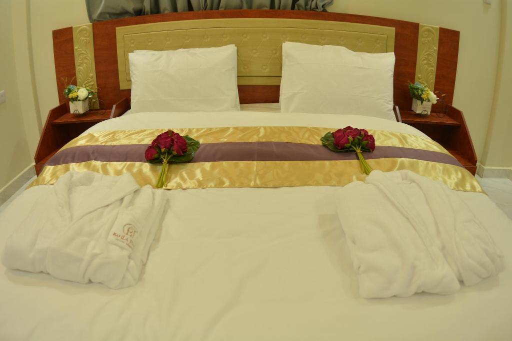 Una cama con toallas blancas y flores. en Bahla Jewel Hotel Apartments, en Bahlāʼ