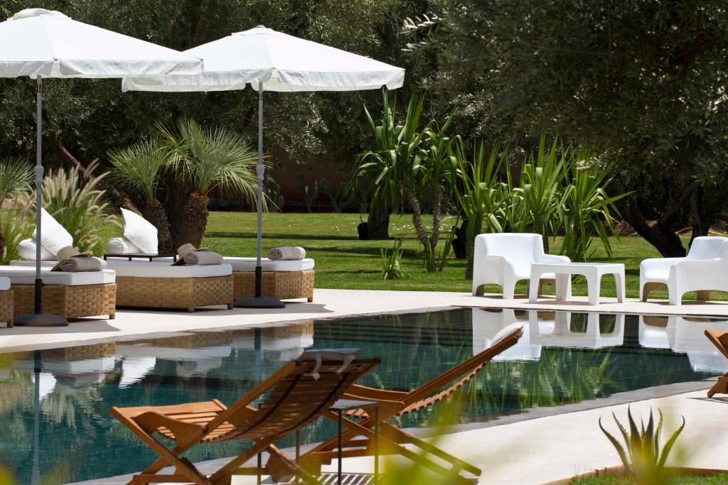 a swimming pool with chairs and umbrellas next to a pool at Hotel Les Cinq Djellabas in Douar Caïd Layadi
