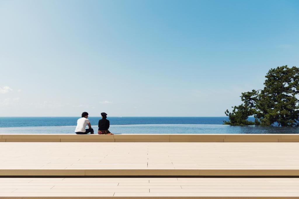 Shirahama Key Terrace Hotel Seamore في شيراهاما: يجلس شخصان على مقعد يطل على المحيط