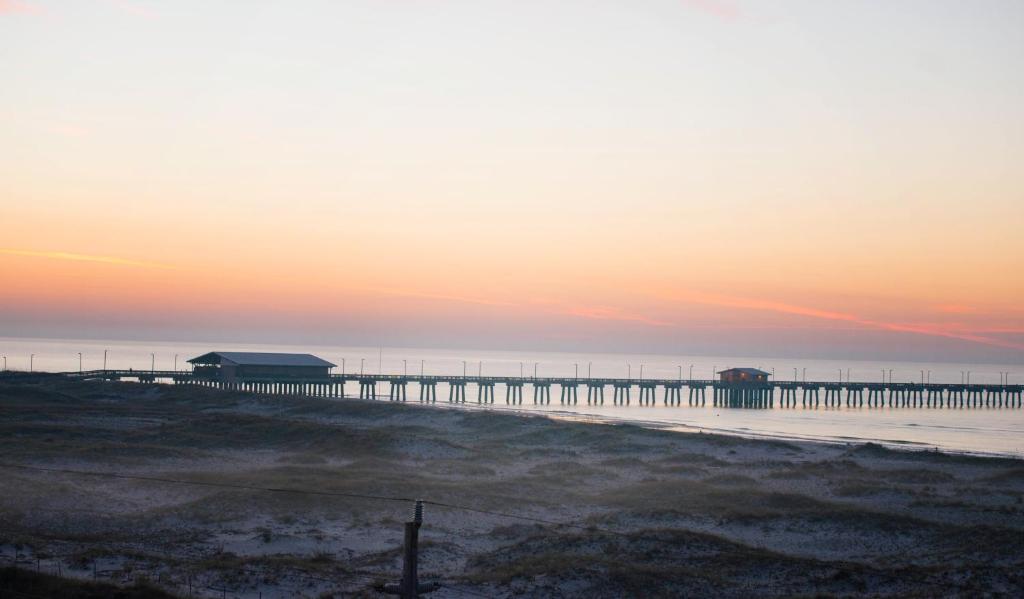 einen Strand mit einem Pier im Wasser bei Sonnenuntergang in der Unterkunft Grand Beach Resort Penthouse 1 in Gulf Shores