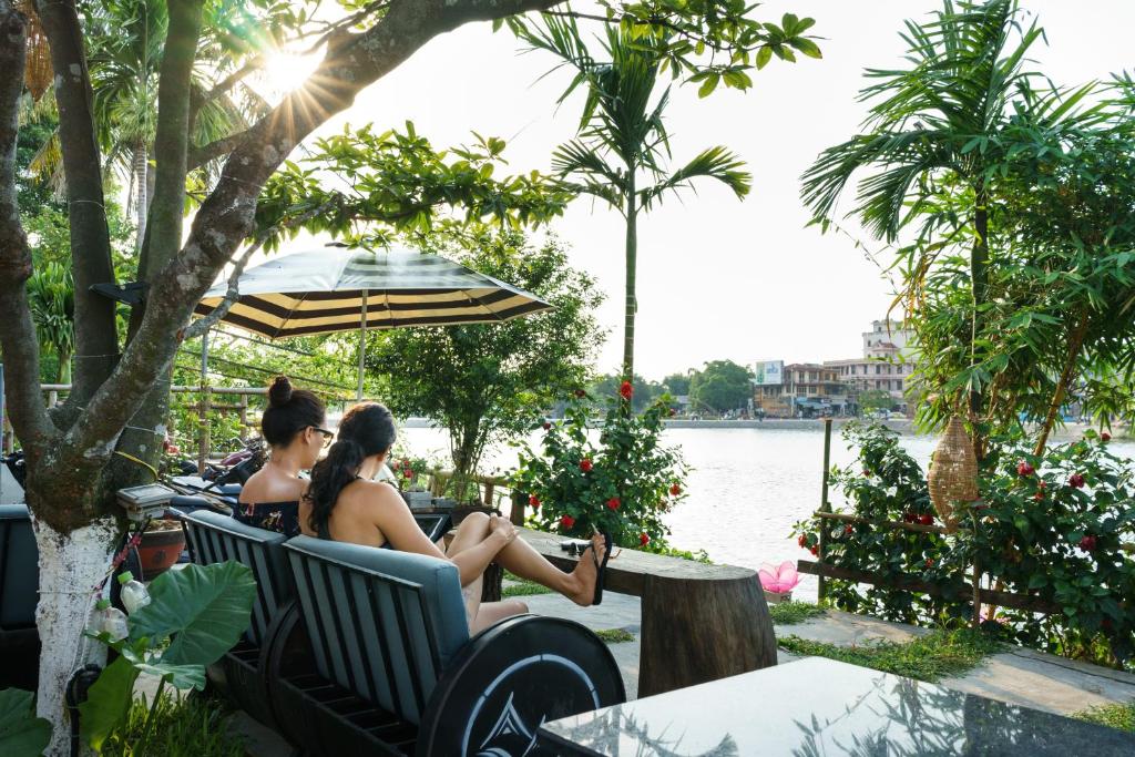 two women sitting on a bench by the water at Hue River Side Villa in Hue