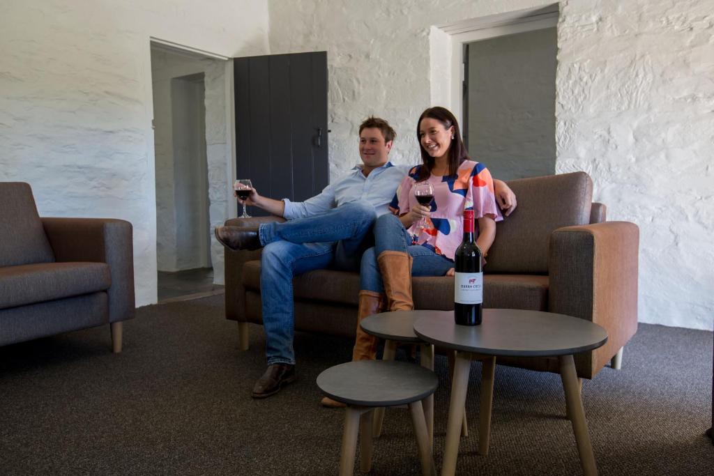 Un uomo e una donna seduti su un divano con una bottiglia di vino di Paxton Square Cottages a Burra