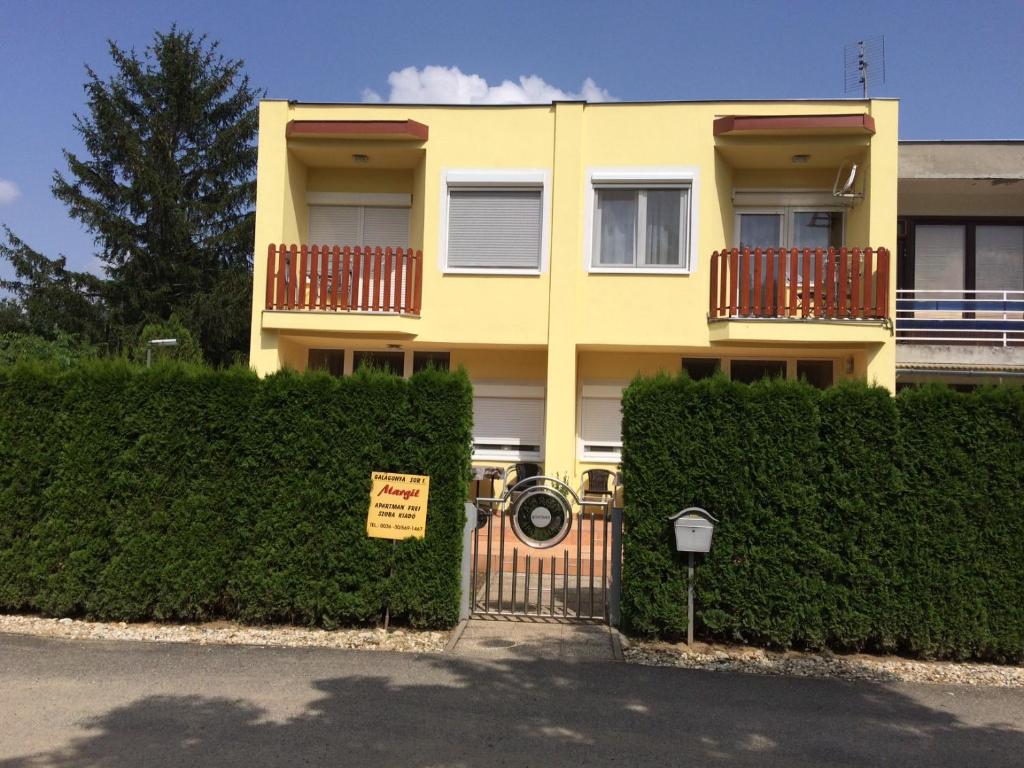 a yellow house with a gate and bushes at Margitapartman in Bük