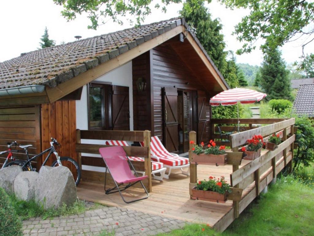 a cabin with a deck with a chair and an umbrella at Nice chalet with dishwasher, in the High Vosges in Le Thillot