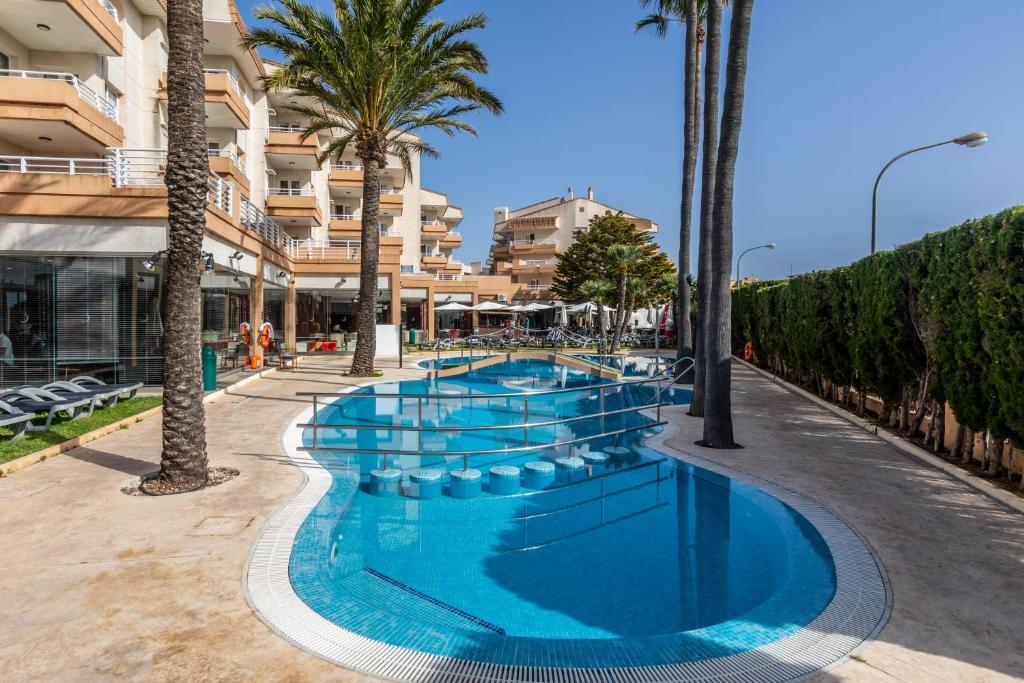 een zwembad met palmbomen en een gebouw bij Hotel Illot Suites in Cala Ratjada