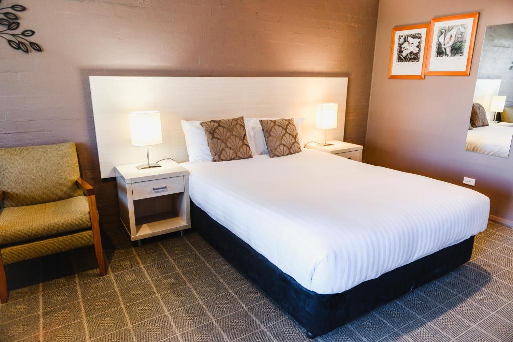 a bedroom with a large white bed and a chair at Balan Village Motel in Nowra