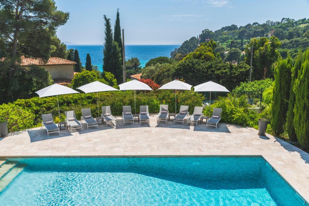 una piscina con sillas y sombrillas y el océano en Les Terrasses du Bailli en Rayol-Canadel-sur-Mer