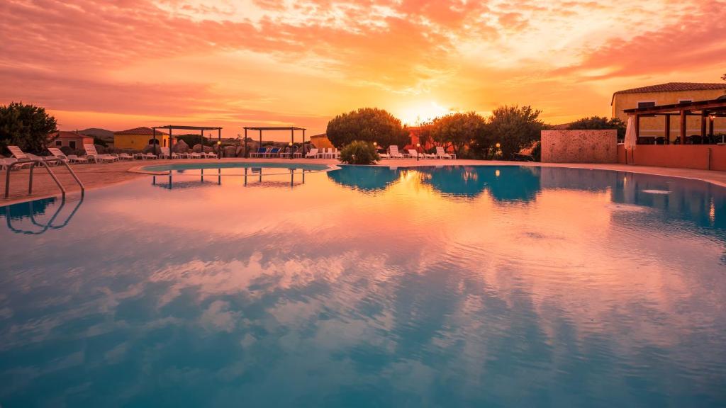 a large swimming pool with a sunset in the background at Residence Lu Lamoni Costa Nord in Aglientu