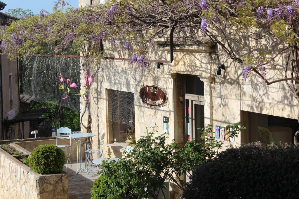 um edifício de pedra com uma mesa e flores roxas em Hôtel de Mirmande em Mirmande