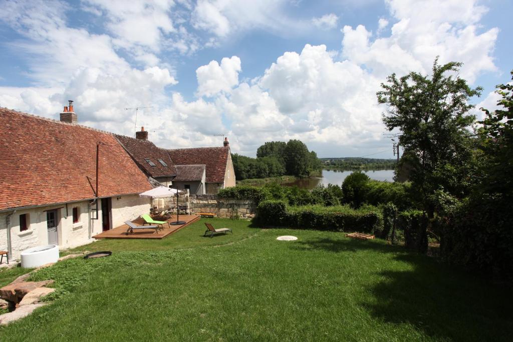 a yard with a house and a lake in the background at Gîte des Cochards in Seigy