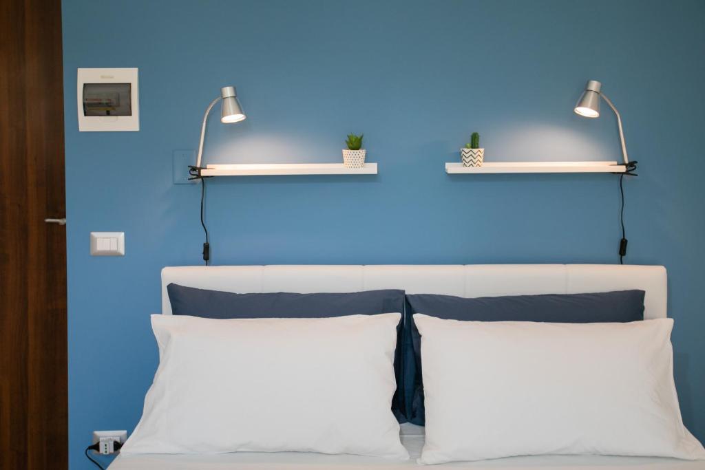 a blue wall with two lights above a bed with pillows at Isola Blu in Siracusa