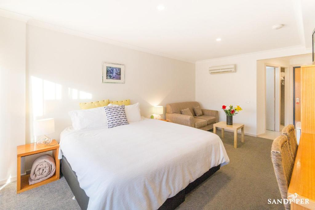 a bedroom with a large white bed and a couch at Sandpiper Motel Apollo Bay in Apollo Bay