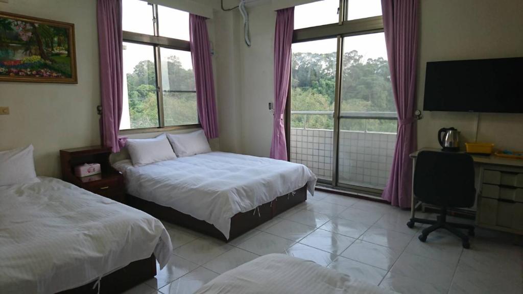 a bedroom with two beds and a desk and windows at Garden Hostel in Minxiong