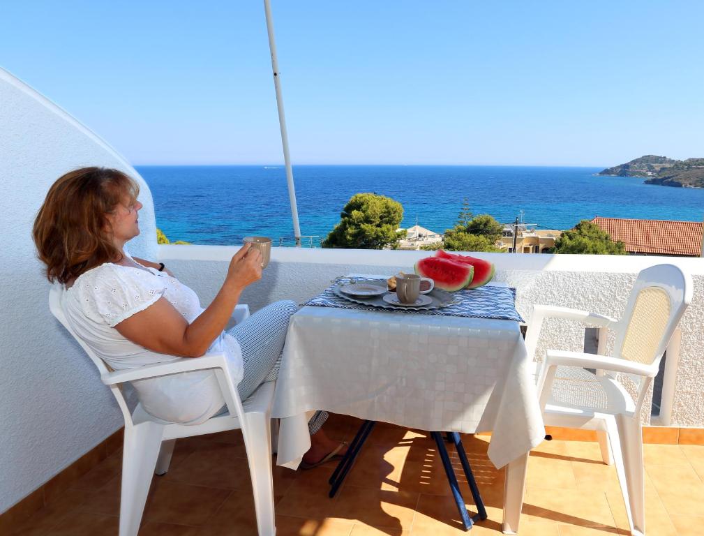 uma mulher sentada numa mesa numa varanda em Yiannis Studios em Agia Marina Aegina