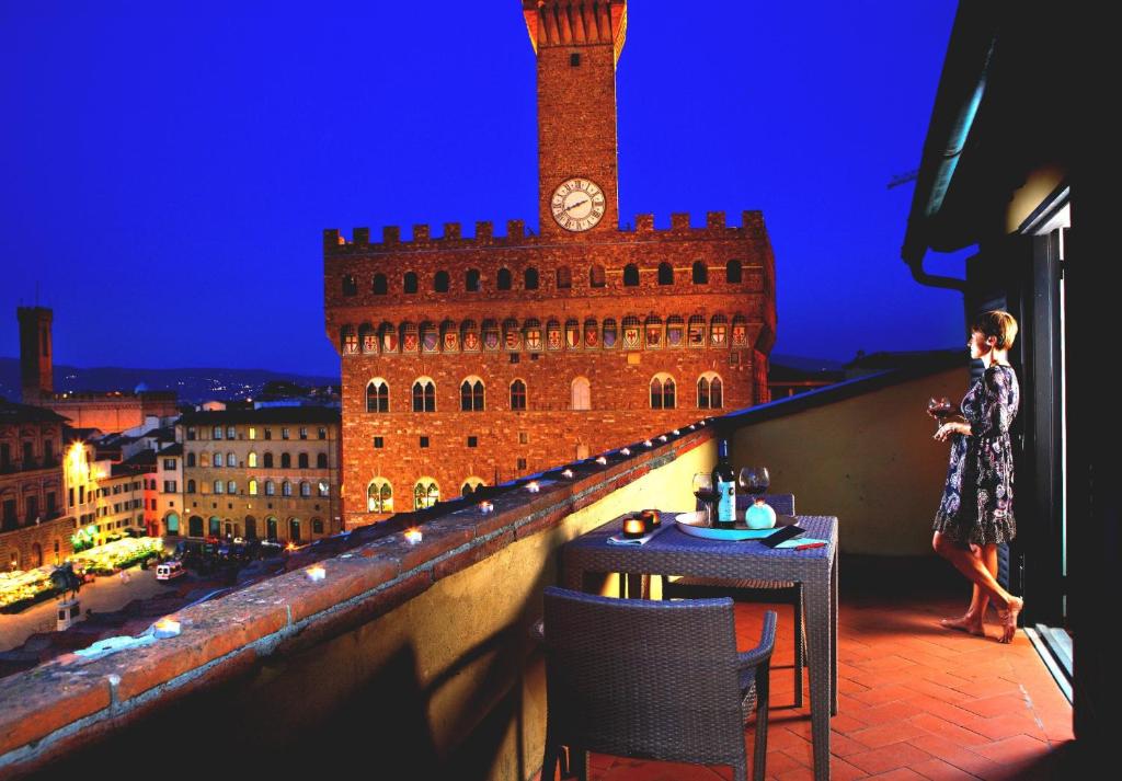 una mujer parada en la parte superior de un balcón con una torre del reloj en Relais Piazza Signoria, en Florencia