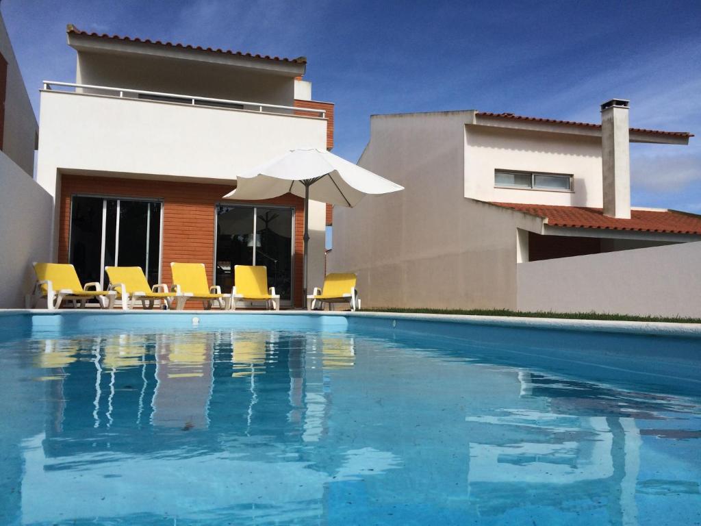 a swimming pool with chairs and an umbrella and a house at Modern Villa in S o Martinho do Porto with Swimming Pool in São Martinho do Porto