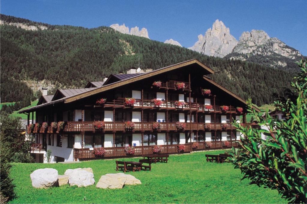a large building with benches in front of a mountain at Residence Anda in Pozza di Fassa