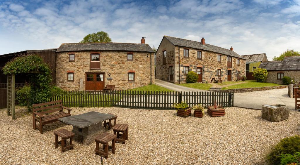 a house with a table and benches and a fence at Tregolls Farm Cottages in Wadebridge