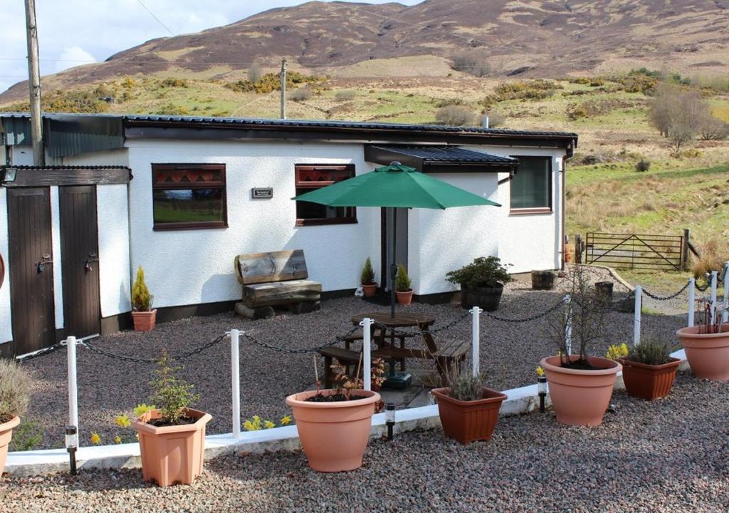 a house with a table and an umbrella and potted plants at Tigh na Freicadan in Spean Bridge