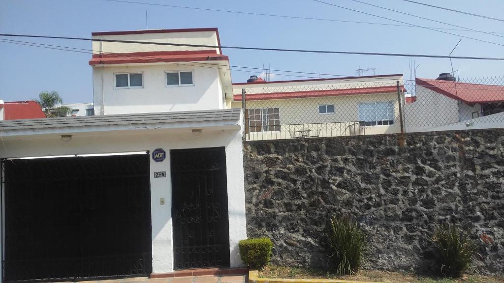 a white house with black doors and a stone wall at Casa privada para descanso, se renta para 8 personas completa Y tambien por habitacion con baño privado para 2 o 4 personas compartiendo areas comunes in Cuernavaca