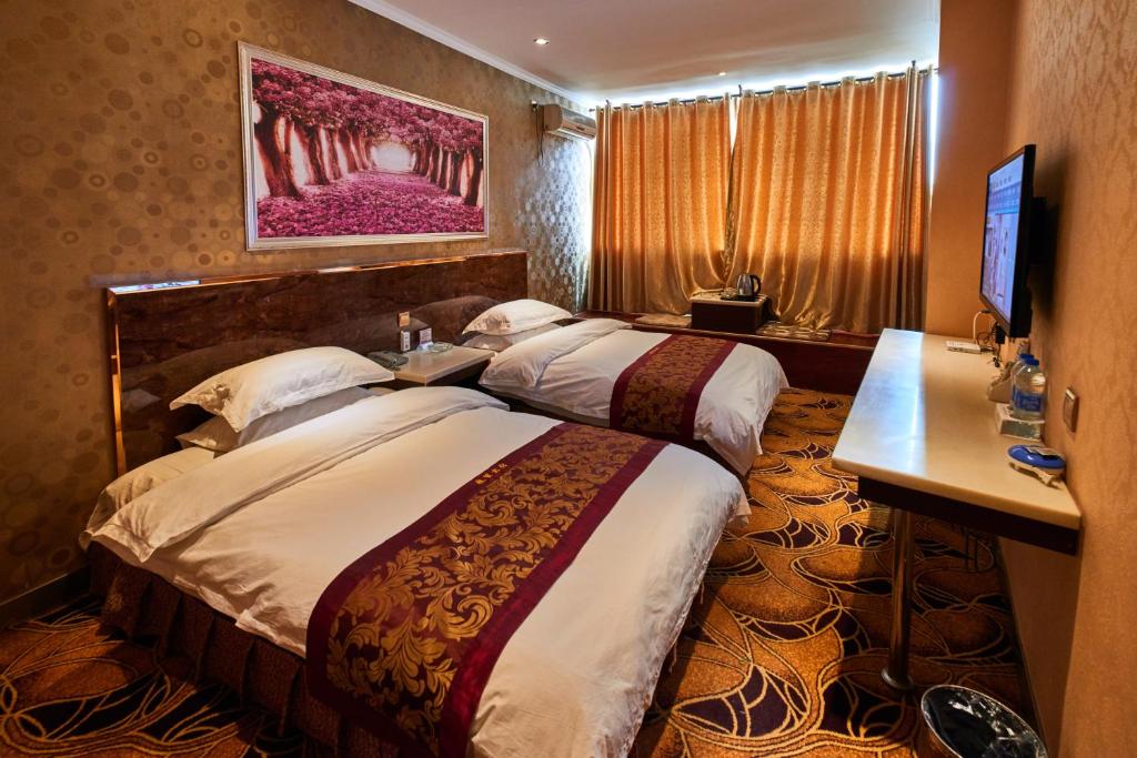 a hotel room with two beds and a television at Zhangye Liangmao Hotel in Zhangye