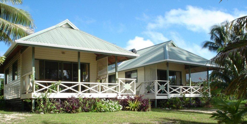 una pequeña casa con porche y palmera en Paparei Beachfront Bungalows, Aitutaki, en Arutanga