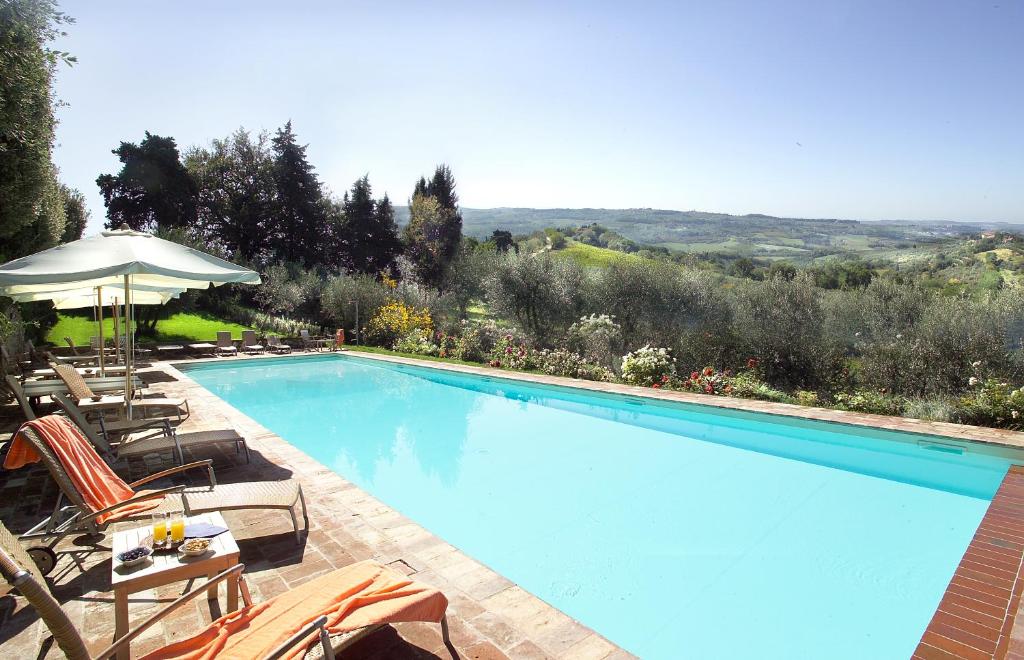 a large swimming pool with chairs and an umbrella at Villa Il Poggiale Dimora Storica in San Casciano in Val di Pesa